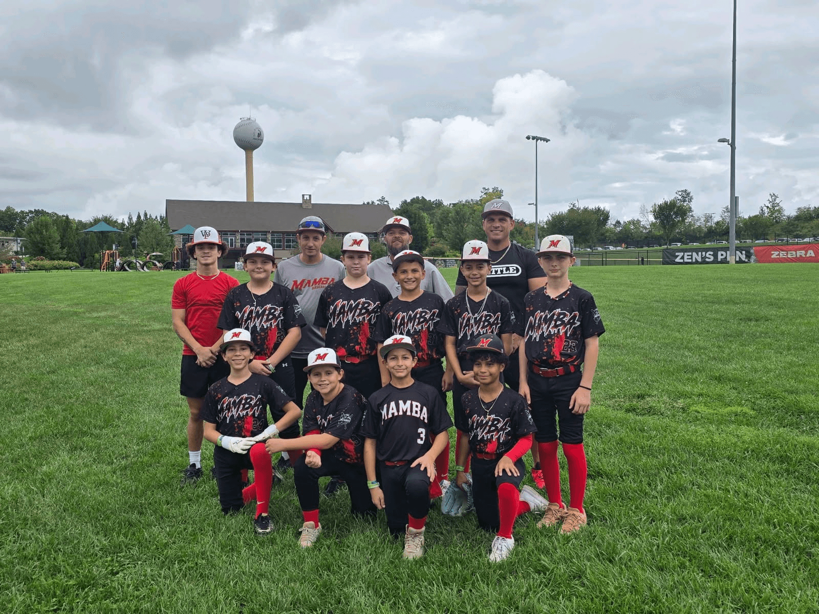 Mamba youth baseball players and coaches wearing black and red custom jerseys with matching baseball caps on the field.